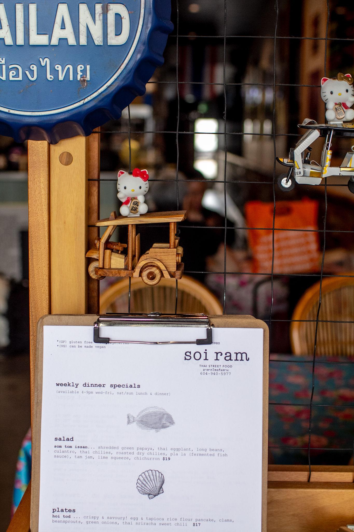 A Hello Kitty figurine riding a wooden tuk-tuk above the weekly specials clipboard