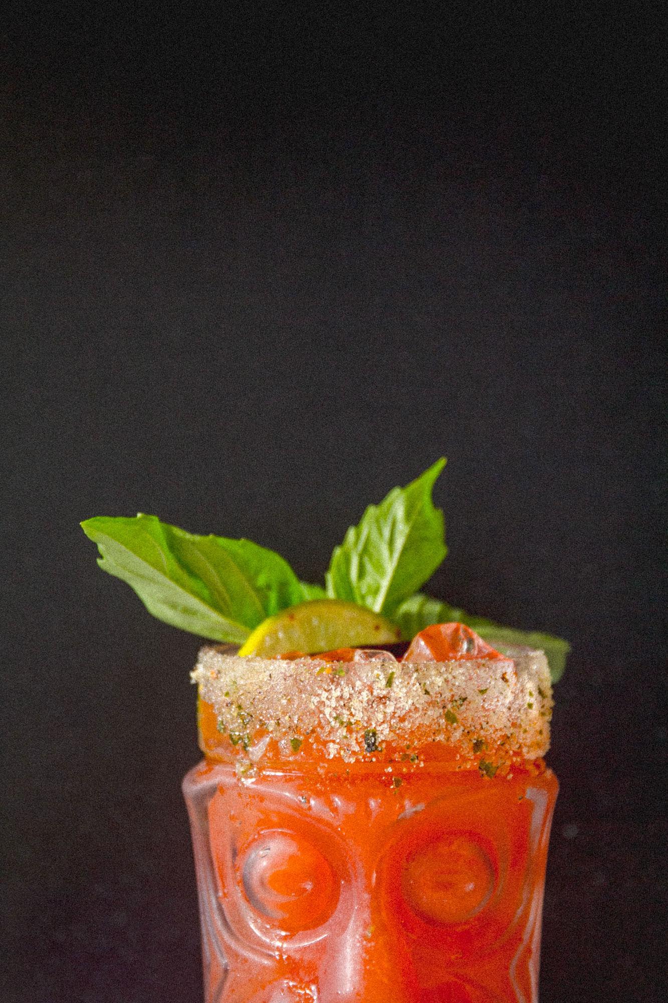 A tiki mug moulded with a face, filled with a red cocktail and topped with Thai basil