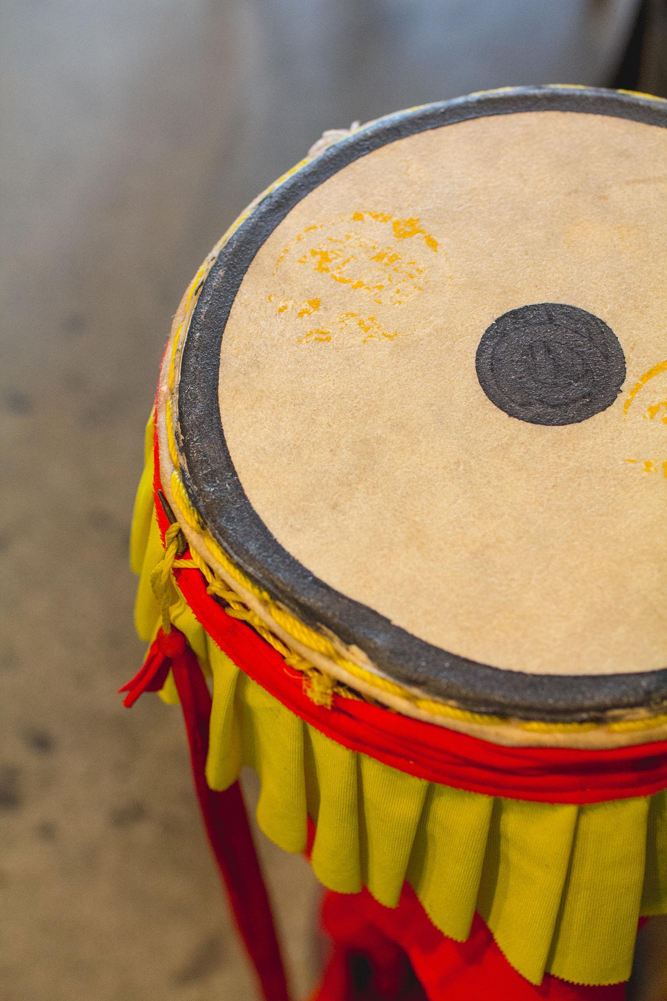 A lion-dance drum with a painted hide head and a yellow and red fabric skirt